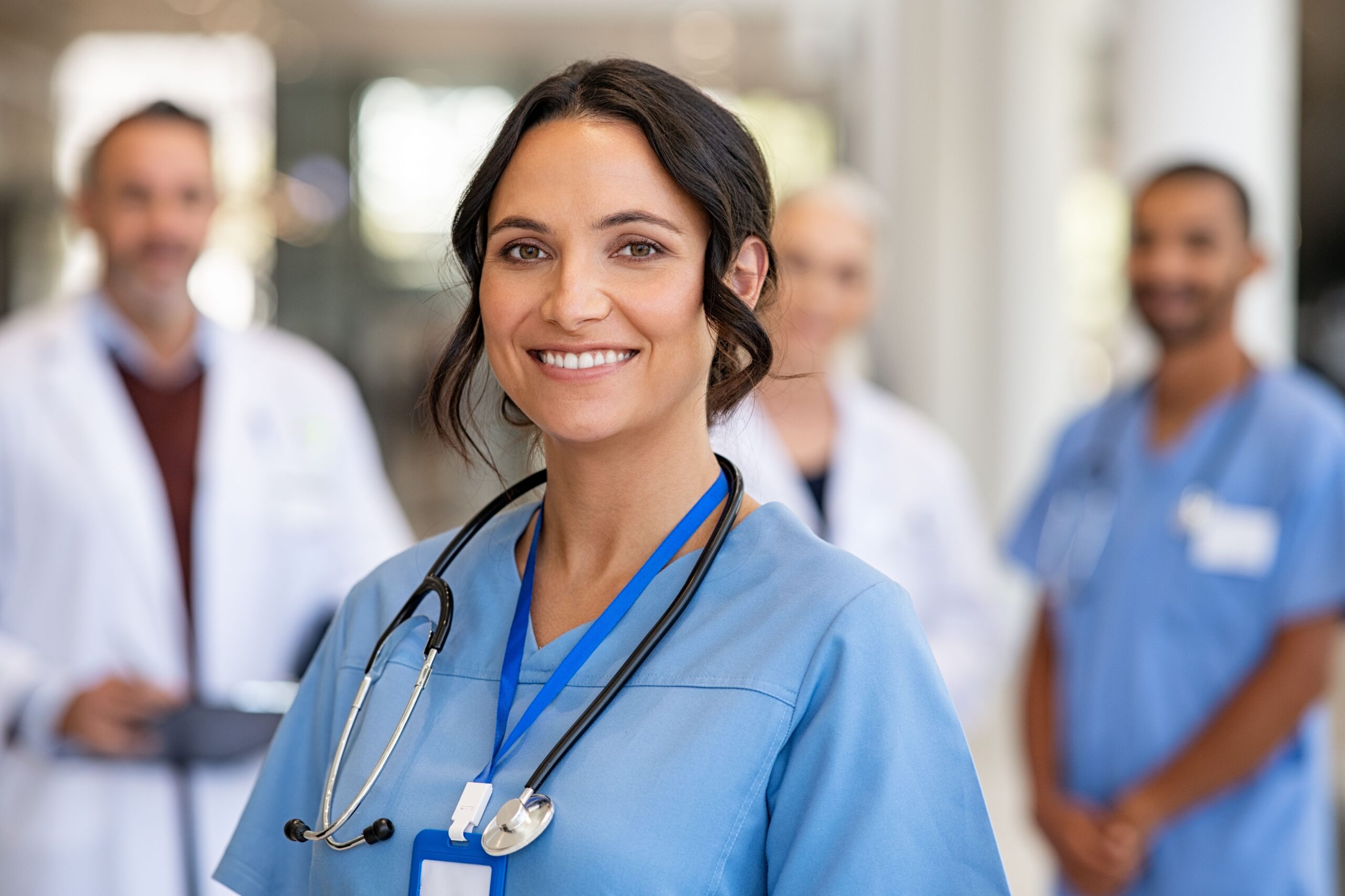 Medical professional wearing a blue scrubs shirt with three others in the background
